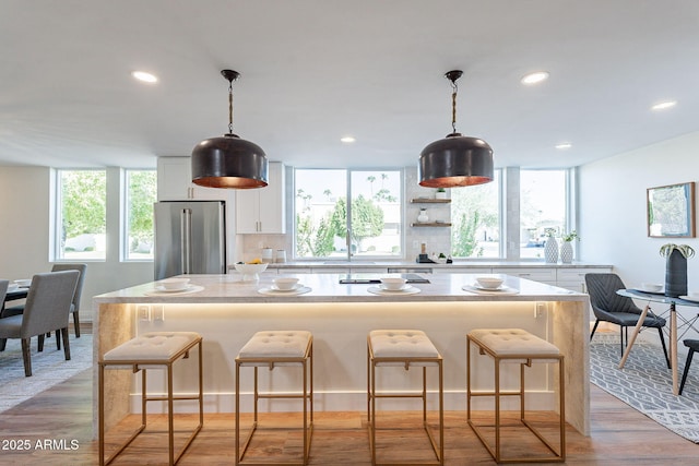 kitchen featuring white cabinetry, a center island, light stone counters, light hardwood / wood-style flooring, and high end fridge