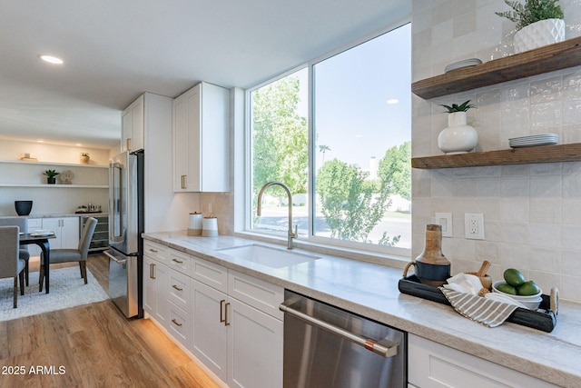 kitchen with sink, light stone countertops, light wood-type flooring, appliances with stainless steel finishes, and white cabinetry