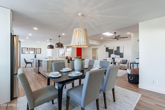 dining room with a skylight, ceiling fan, and light hardwood / wood-style flooring