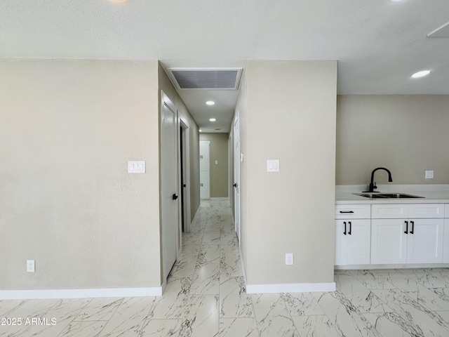 corridor with marble finish floor, visible vents, a sink, and baseboards