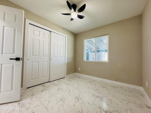 unfurnished bedroom with marble finish floor, a ceiling fan, baseboards, and a closet