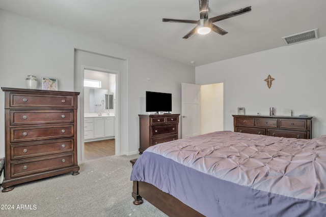 bedroom with ceiling fan, light colored carpet, and ensuite bath