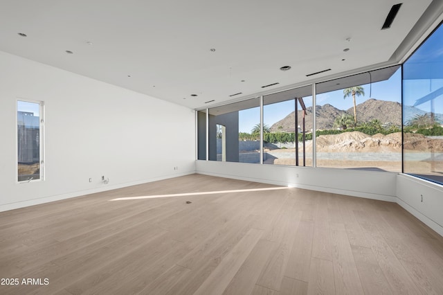 spare room featuring light wood-type flooring, a mountain view, and baseboards