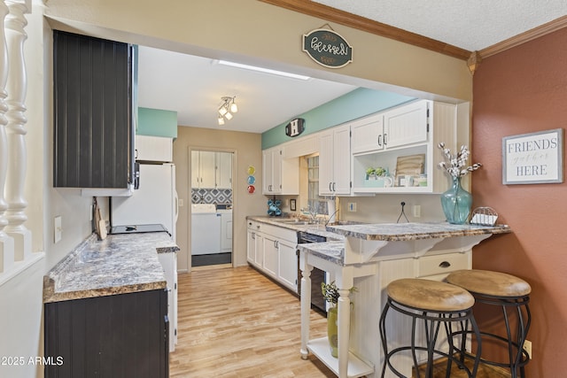 kitchen with a breakfast bar, white cabinetry, dishwashing machine, independent washer and dryer, and crown molding