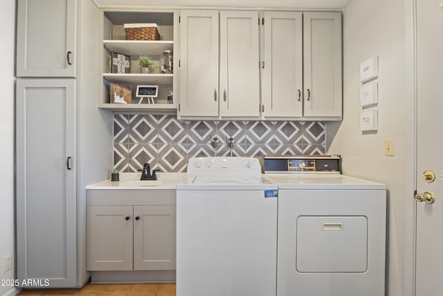 clothes washing area with separate washer and dryer, sink, and cabinets