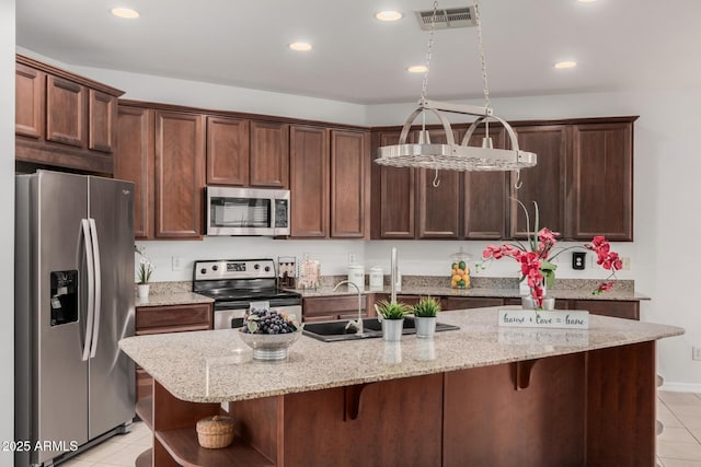 kitchen featuring stainless steel appliances, visible vents, a center island with sink, and light stone counters