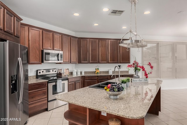 kitchen featuring appliances with stainless steel finishes, light stone counters, sink, light tile patterned floors, and a center island with sink