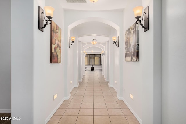 hallway with arched walkways, baseboards, and light tile patterned floors