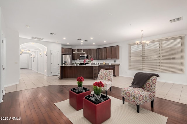 living area with a chandelier, arched walkways, light wood-type flooring, and visible vents