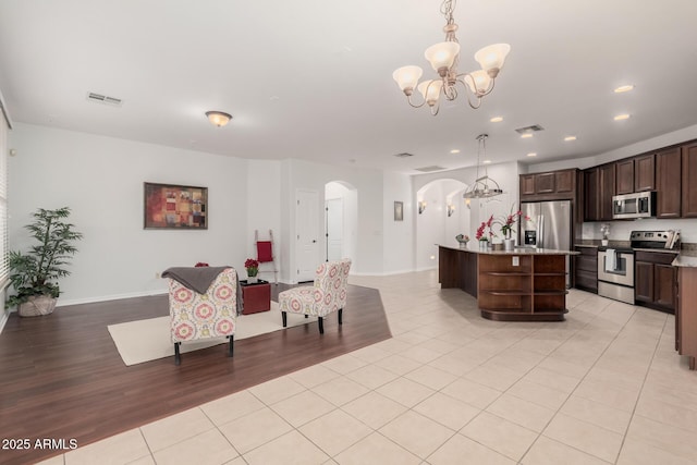 kitchen with stainless steel appliances, arched walkways, a kitchen island, and hanging light fixtures