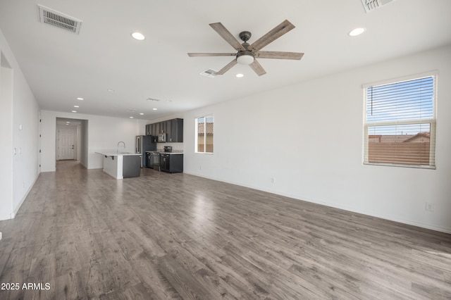 unfurnished living room featuring hardwood / wood-style flooring, sink, and ceiling fan