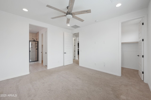 unfurnished bedroom with ensuite bath, a spacious closet, light colored carpet, a closet, and ceiling fan