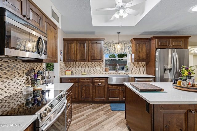 kitchen featuring visible vents, a ceiling fan, a sink, a tray ceiling, and appliances with stainless steel finishes