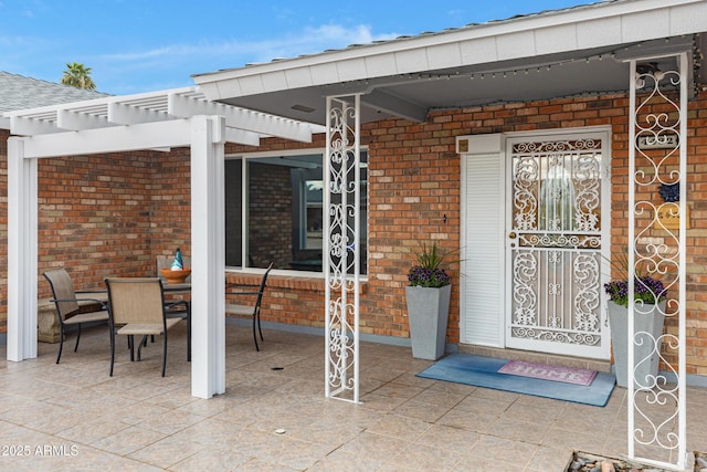 property entrance with outdoor dining area, brick siding, and a pergola