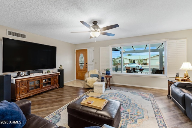 living room with wood finished floors, a ceiling fan, visible vents, and a textured ceiling