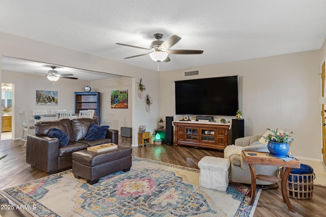 living room featuring wood finished floors, baseboards, a ceiling fan, visible vents, and a textured ceiling