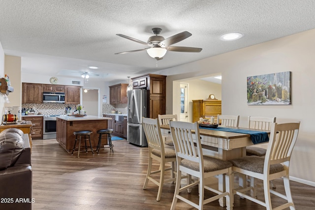 dining room with a ceiling fan, visible vents, baseboards, dark wood-style flooring, and a textured ceiling