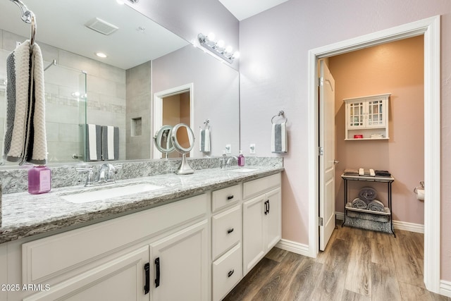 bathroom with double vanity, a shower stall, a sink, and wood finished floors