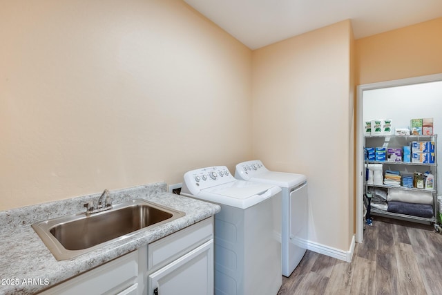 laundry room with light wood finished floors, cabinet space, a sink, independent washer and dryer, and baseboards