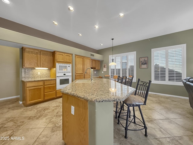 kitchen featuring pendant lighting, sink, white appliances, a breakfast bar area, and an island with sink