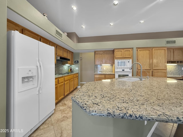 kitchen with sink, white appliances, light stone countertops, a kitchen island with sink, and decorative backsplash