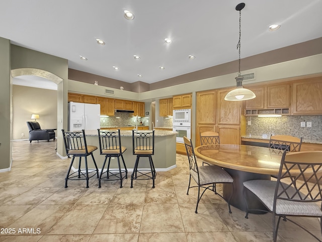 kitchen with pendant lighting, white appliances, a kitchen island, a kitchen bar, and decorative backsplash