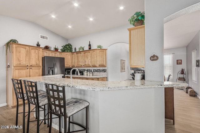 kitchen featuring a breakfast bar, backsplash, kitchen peninsula, vaulted ceiling, and black fridge with ice dispenser