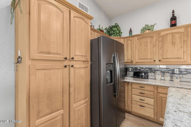 kitchen with light stone countertops, stainless steel refrigerator with ice dispenser, backsplash, light wood-type flooring, and light brown cabinets