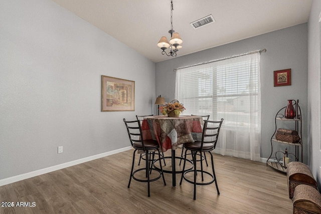 dining space featuring hardwood / wood-style flooring, vaulted ceiling, and a notable chandelier