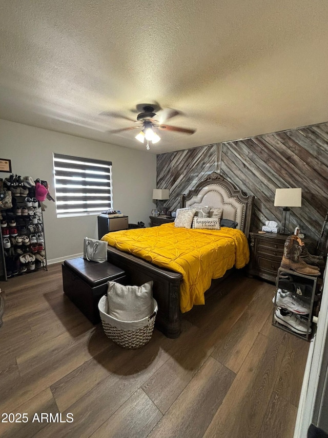 bedroom featuring ceiling fan, a textured ceiling, dark hardwood / wood-style floors, and wooden walls