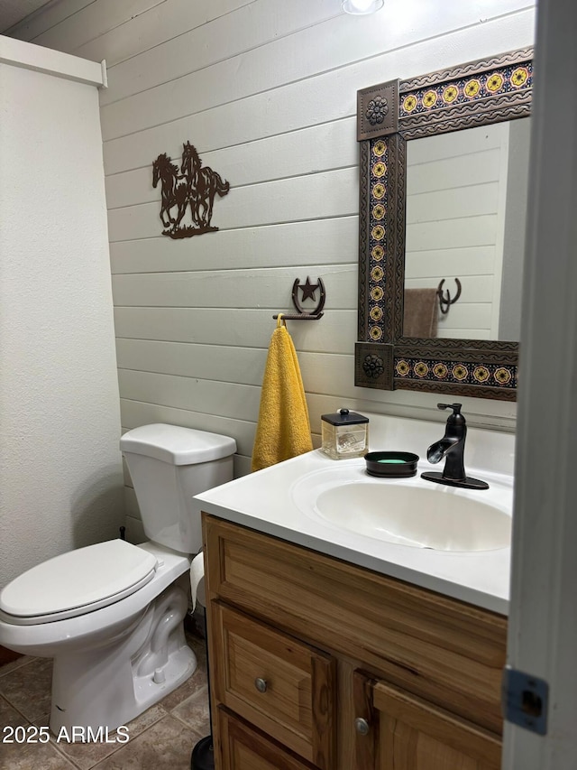 bathroom with toilet, wood walls, and vanity