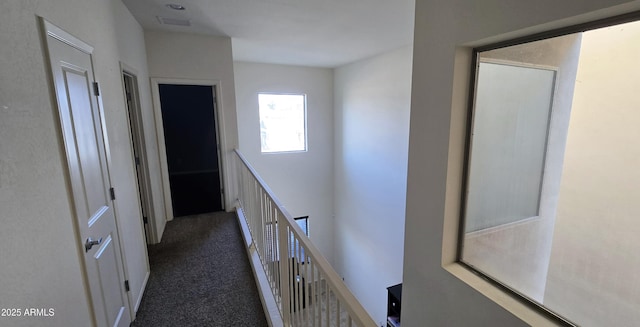 corridor with visible vents, dark carpet, and an upstairs landing