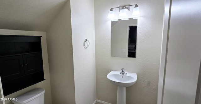 bathroom with toilet, a textured ceiling, and a textured wall