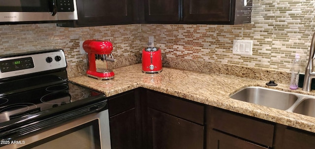 kitchen featuring tasteful backsplash, appliances with stainless steel finishes, light stone countertops, dark brown cabinets, and a sink