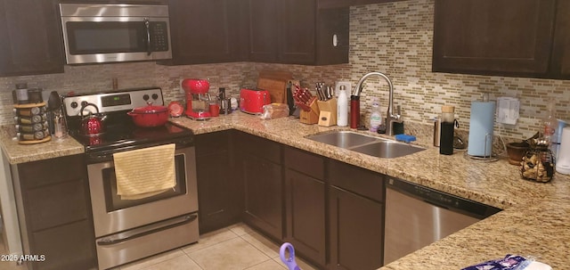 kitchen with stainless steel appliances, a sink, decorative backsplash, and light stone countertops