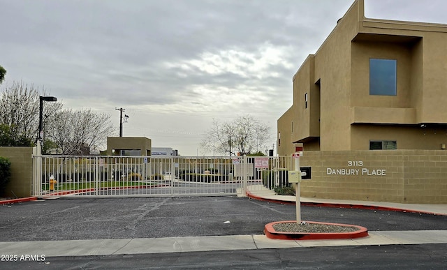 view of road featuring a gate, a gated entry, street lights, and curbs