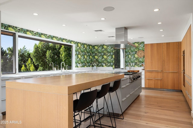 kitchen featuring a breakfast bar, a spacious island, wall oven, light hardwood / wood-style floors, and stainless steel gas stovetop