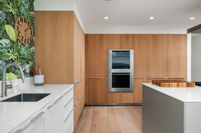 kitchen featuring sink, double oven, and light wood-type flooring