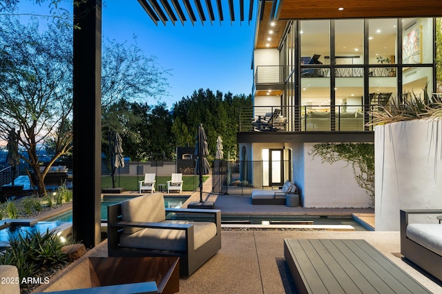 patio terrace at dusk with a balcony, an outdoor living space, and a fenced in pool