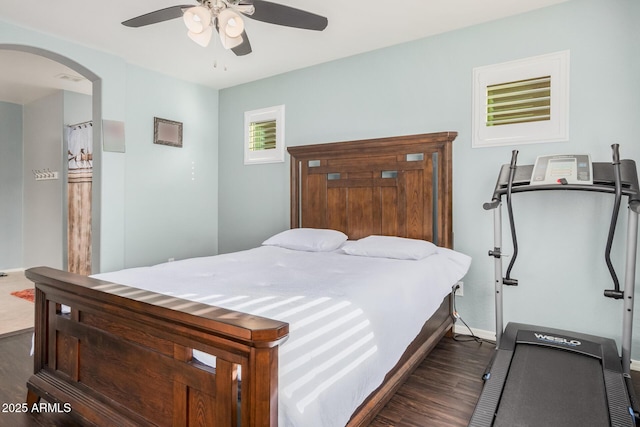 bedroom with dark wood-style floors, arched walkways, baseboards, and a ceiling fan