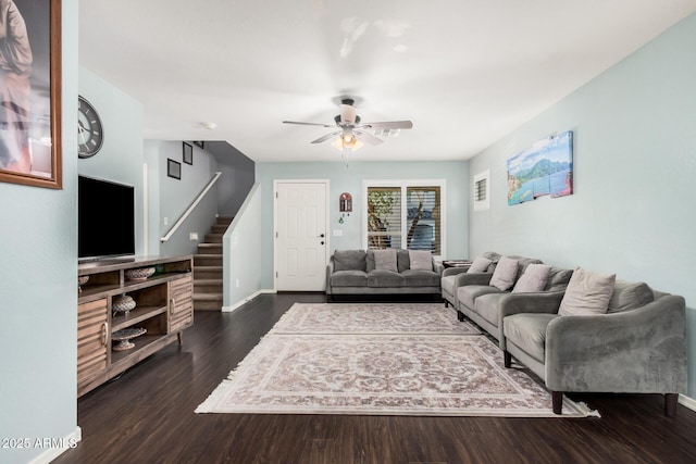 living room with stairs, ceiling fan, dark wood-style floors, and baseboards