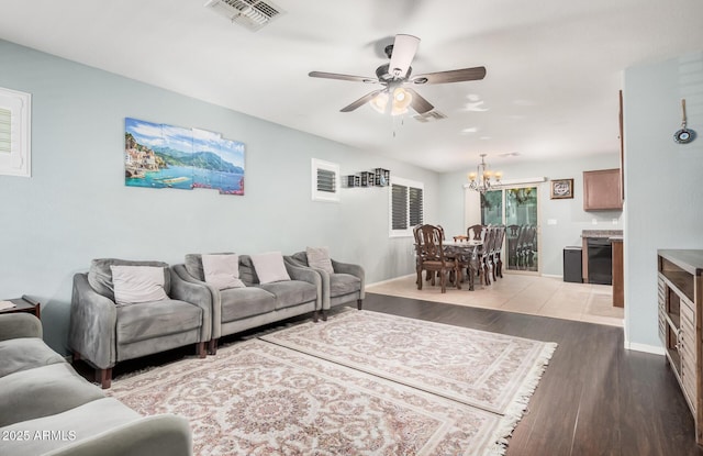 living room featuring ceiling fan with notable chandelier, visible vents, baseboards, and wood finished floors