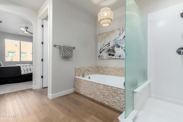 bathroom with ceiling fan, a relaxing tiled tub, and hardwood / wood-style flooring