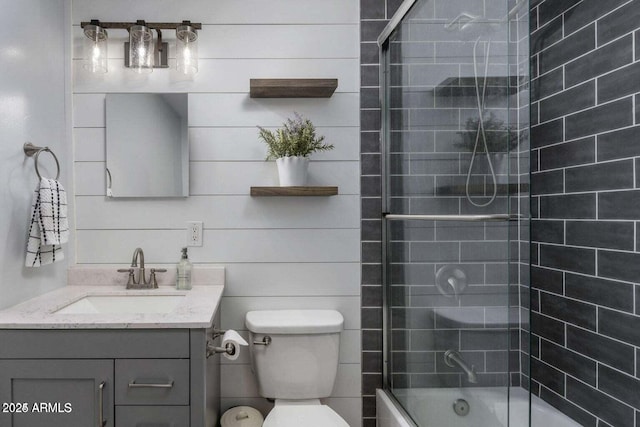 full bathroom with wood walls, vanity, bath / shower combo with glass door, and toilet