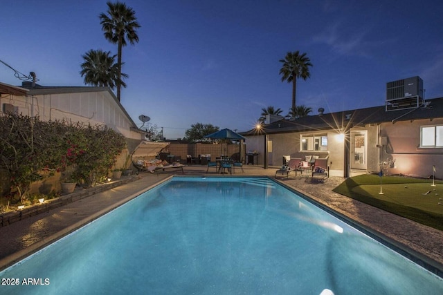 pool at dusk with central air condition unit and a patio