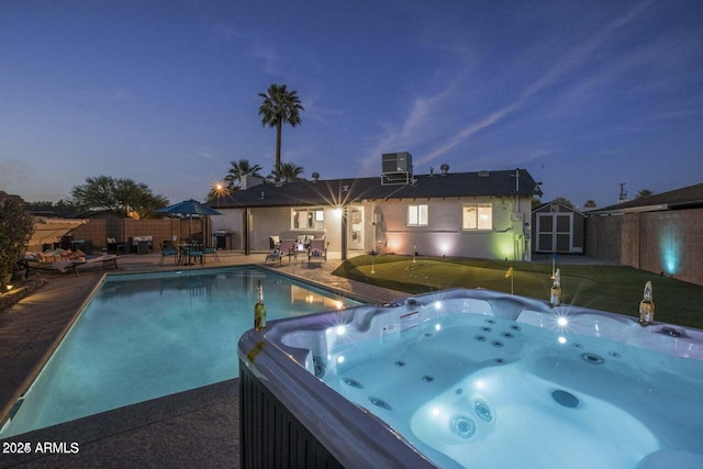 pool at dusk featuring a patio, a hot tub, a storage unit, and central air condition unit