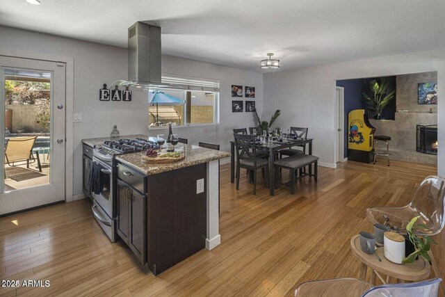 kitchen featuring light wood-type flooring, light stone counters, dark brown cabinets, island range hood, and stainless steel range with gas cooktop