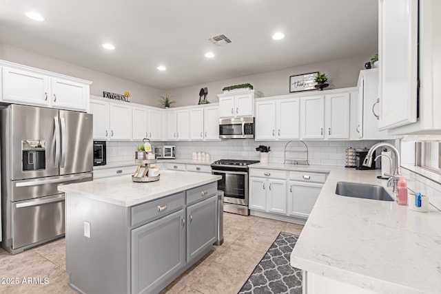 kitchen with a kitchen island, gray cabinets, a sink, decorative backsplash, and appliances with stainless steel finishes