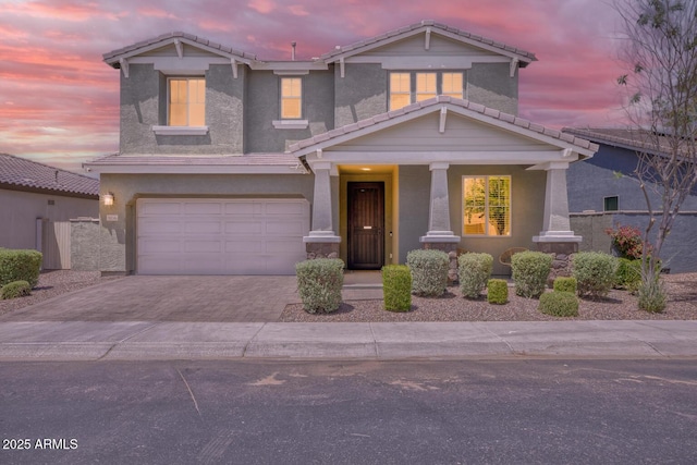 view of front facade featuring a tile roof, driveway, an attached garage, stucco siding, and covered porch