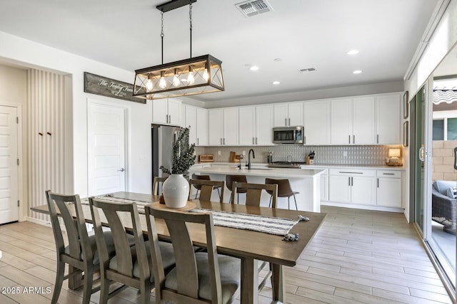 kitchen with appliances with stainless steel finishes, light countertops, decorative backsplash, light wood finished floors, and white cabinetry